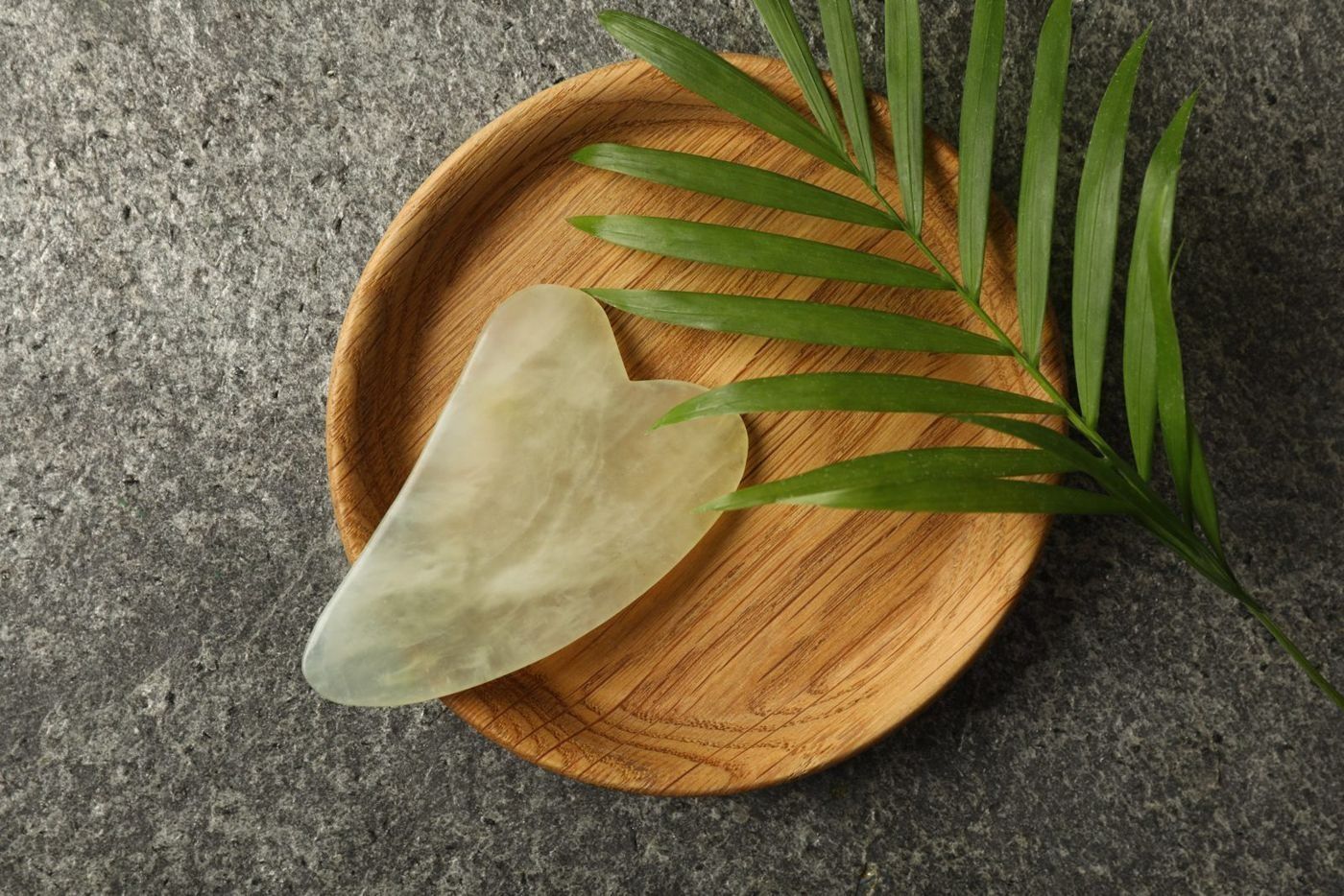 A jade gua sha stone on a wooden dish